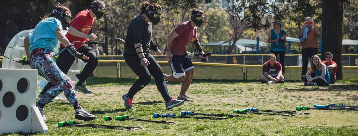 Masked Archery Tag players running onto an outdoor playing field